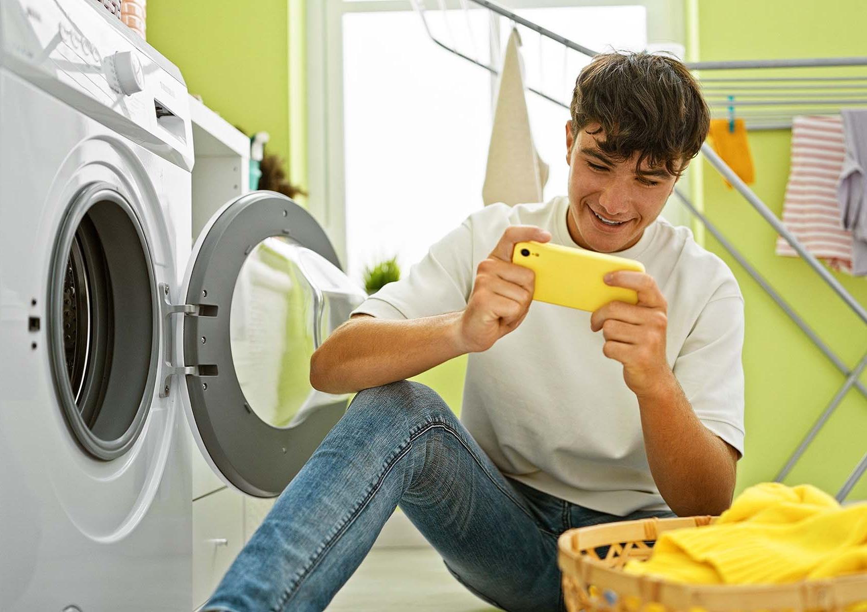 A teenager on their phone while doing laundry